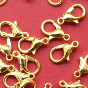 May include: A group of gold-toned metal lobster claw clasps scattered on a red surface. These clasps are commonly used for jewelry making and crafting.