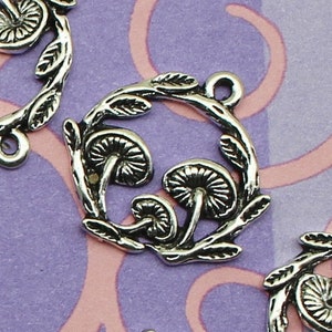 May include: Silver charm pendants with a mushroom design. Each charm features three mushrooms with a leafy wreath around them.