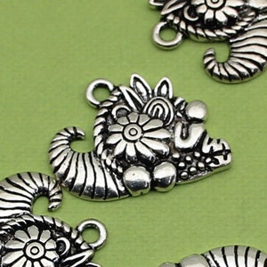 May include: Silver tone metal charms with a floral design and a curled horn shape. The charms have a detailed design and are perfect for jewelry making or crafting.