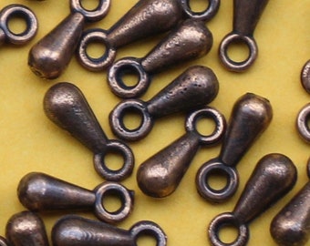 May include: A group of small, teardrop-shaped metal charms with a loop at the top. The charms are a copper color and are scattered on a yellow surface.