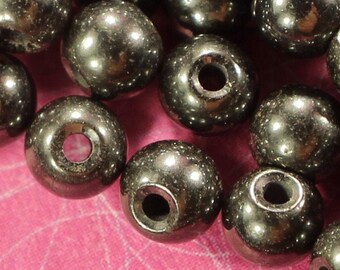 May include: A close-up of a pile of black round beads. The beads are smooth and shiny, and they are arranged in a random pattern.