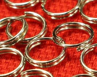 May include: A close-up of a large quantity of silver jump rings on a red fabric surface. The rings are all the same size and are arranged in a random pattern.