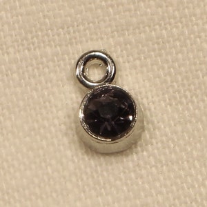 May include: A silver charm with a small, round, dark purple gemstone.