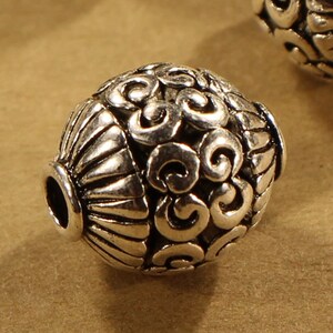 May include: Silver metal beads with a decorative swirl pattern. The beads have a hole in the center for stringing.