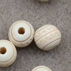 May include: A collection of white wooden beads with a gold-colored design. The beads have a hole in the center for stringing.