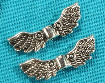 May include: Silver metal wing-shaped jewelry clasps with a textured surface. The clasps are arranged in a pattern on a turquoise blue fabric background.