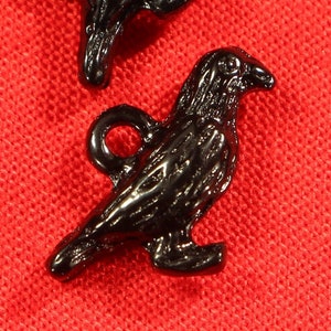 May include: Two black metal crow charms with a detailed design. The charms have a loop at the top for attaching to a necklace, bracelet, or other jewellery.