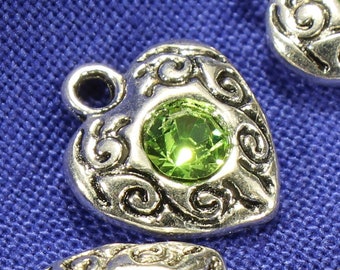 May include: Four silver heart-shaped charms with ornate designs and green gem accents.