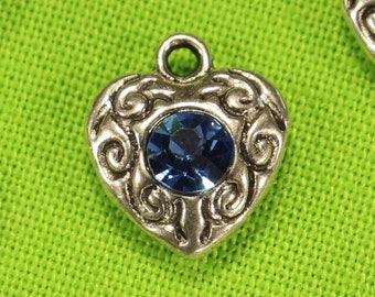 May include: A group of silver heart-shaped charms with blue rhinestones. Each charm has a decorative design around the edge.