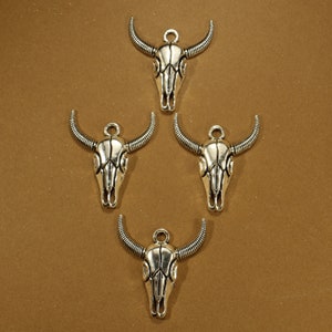 May include: Four silver skull charms with a detailed design. Each charm has a loop at the top for attaching to a necklace or bracelet.