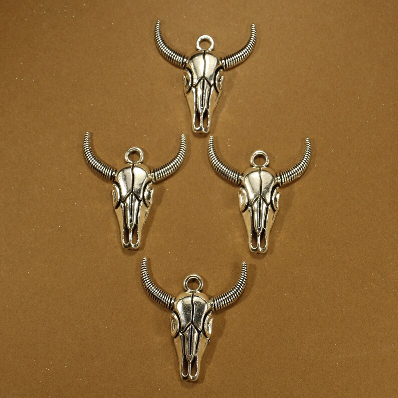 May include: Four silver skull charms with a detailed design. Each charm has a loop at the top for attaching to a necklace or bracelet.