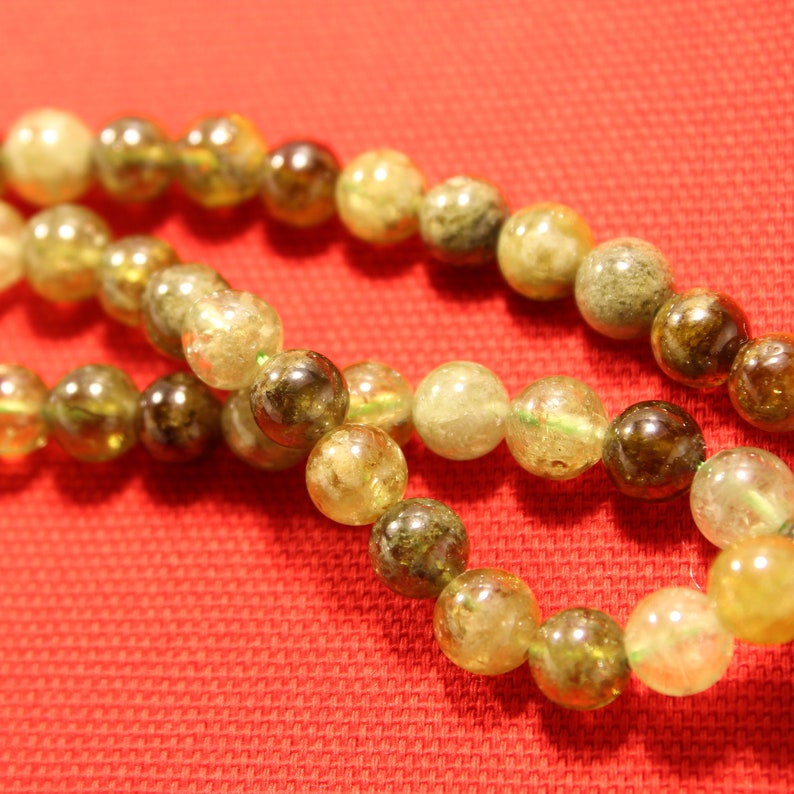 May include: A strand of green and yellow gemstone beads. The beads are round and have a natural, unpolished look.