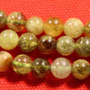 May include: A strand of green and yellow gemstone beads. The beads are round and have a translucent appearance.