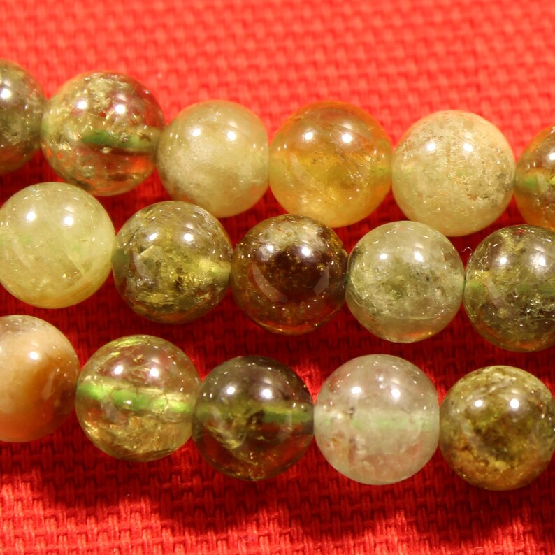May include: A strand of green and yellow gemstone beads. The beads are round and have a translucent appearance.