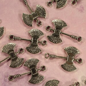 May include: Silver-toned metal axe charms with intricate designs. The charms have a double-headed axe shape with a loop at the top for attaching to jewelry or crafts.