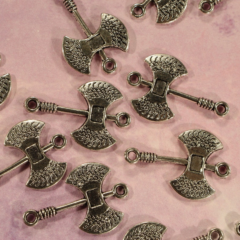 May include: Silver-toned metal axe charms with intricate designs. The charms have a double-headed axe shape with a loop at the top for attaching to jewelry or crafts.