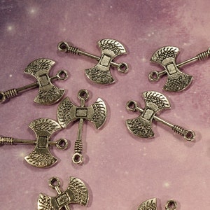 May include: A collection of eight silver-toned axe charms with intricate details. The charms are designed with a double-headed axe shape and have a loop at the top for attaching to jewelry or other crafts.