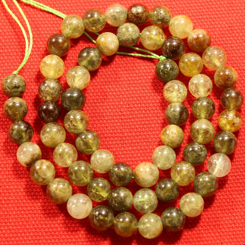 May include: A strand of green and brown gemstone beads. The beads are round and have a translucent appearance. The beads are strung on a green cord.