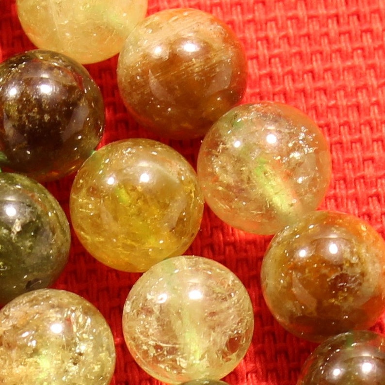 May include: A close-up of a strand of round, translucent green and yellow beads. The beads are made of natural stone and have a slightly rough texture.