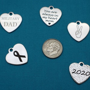 May include: Five silver heart-shaped charms with different engravings. The charms include "Military Dad", "You are always in my heart mom", a peace sign, a black ribbon, and "2020" with a geometric pattern.