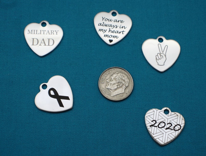 May include: Five silver heart-shaped charms with different engravings. The charms include "Military Dad", "You are always in my heart mom", a peace sign, a black ribbon, and "2020" with a geometric pattern.