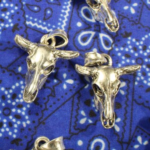 May include: Two silver bull skull pendants with intricate details. The pendants are on a blue bandana background.