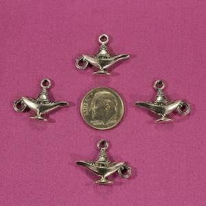 May include: Four silver-toned genie lamp charms with intricate details. The charms are arranged in a square pattern on a purple background.