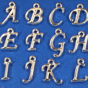 May include: Silver-toned metal alphabet letter charms, each letter is in a cursive font style. The letters are A, B, C, D, E, F, G, H, I, J, K, and L.