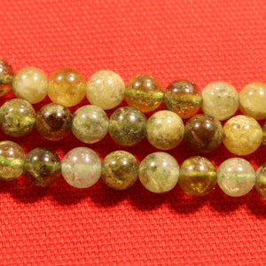 May include: A strand of green and yellow gemstone beads. The beads are round and have a translucent appearance. The beads are strung on a clear thread.