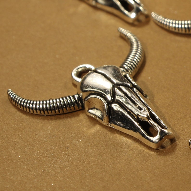 May include: Silver-toned metal bull skull charm with detailed horns and a textured surface.