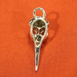 May include: Silver pendant charm in the shape of a bird skull with a long beak. The pendant is detailed with intricate carvings and has a loop at the top for attaching to a chain.