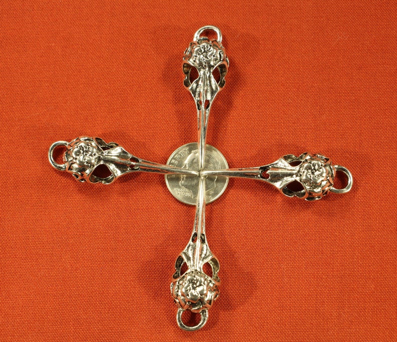 May include: Four silver-toned metal bird skull charms with floral details. The charms are arranged in a cross shape with a silver-toned coin in the center.