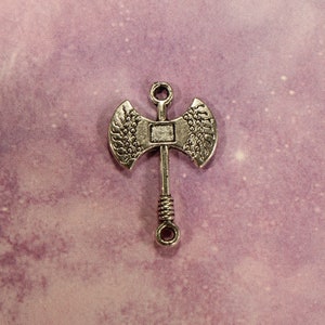 May include: Silver-toned metal axe charm with a detailed design. The axe has a double-headed blade and a twisted handle.