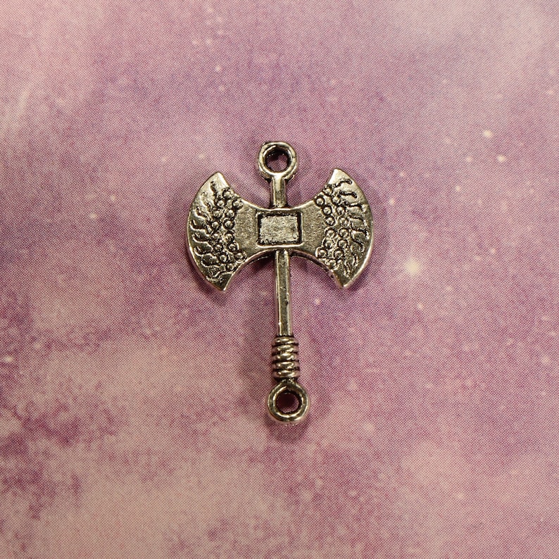May include: Silver-toned metal axe charm with a detailed design. The axe has a double-headed blade and a twisted handle.