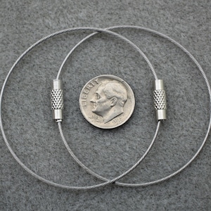 Puede incluir: Dos llaveros plateados con un dise&ntilde;o de cable y tapas de extremo plateadas. Los llaveros est&aacute;n dispuestos sobre una superficie gris texturizada.