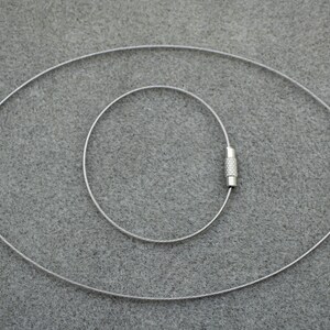 Puede incluir: Tres cadenas de cable de metal plateado con extremos crimpados. Las cadenas est&aacute;n dispuestas en c&iacute;rculos conc&eacute;ntricos.