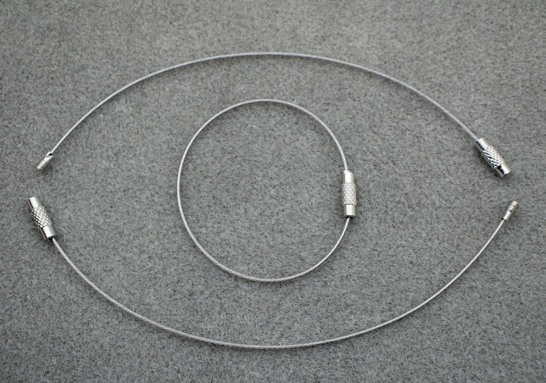 Puede incluir: Tres cadenas de cable de metal plateado con extremos crimpados. Las cadenas est&aacute;n dispuestas en c&iacute;rculos conc&eacute;ntricos.