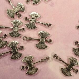 May include: A collection of silver-toned axe charms with intricate details. Each charm features a double-headed axe design with a loop for attaching to jewelry or other crafts.