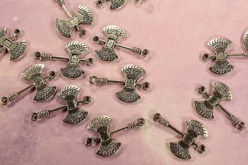 May include: A collection of silver-toned axe charms with intricate details. Each charm features a double-headed axe design with a loop for attaching to jewelry or other crafts.