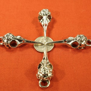 May include: Four silver bird skull charms arranged in a cross shape. The charms are detailed with intricate carvings and have a loop at the top for attaching to jewelry.