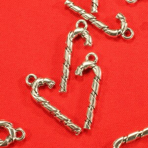 Op de afbeelding: Zilverkleurige snoepstok charms met een gedraaid ontwerp. De charms zijn op een rode achtergrond.