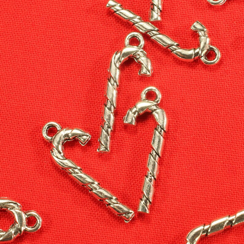 Op de afbeelding: Zilverkleurige snoepstok charms met een gedraaid ontwerp. De charms zijn op een rode achtergrond.