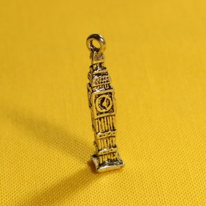May include: Silver charm shaped like Big Ben, the famous clock tower in London, England. The charm is detailed with a clock face and a pointed roof.