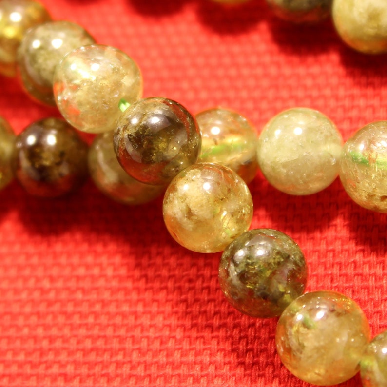 May include: A strand of green and yellow gemstone beads. The beads are round and have a smooth, polished finish.