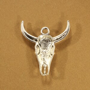 May include: Silver-toned metal charm in the shape of a bull skull with horns.