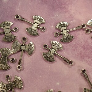 May include: A collection of silver-toned axe charms with intricate details. The charms have a double-sided axe head design with a loop at the top for attaching to jewelry or crafts.