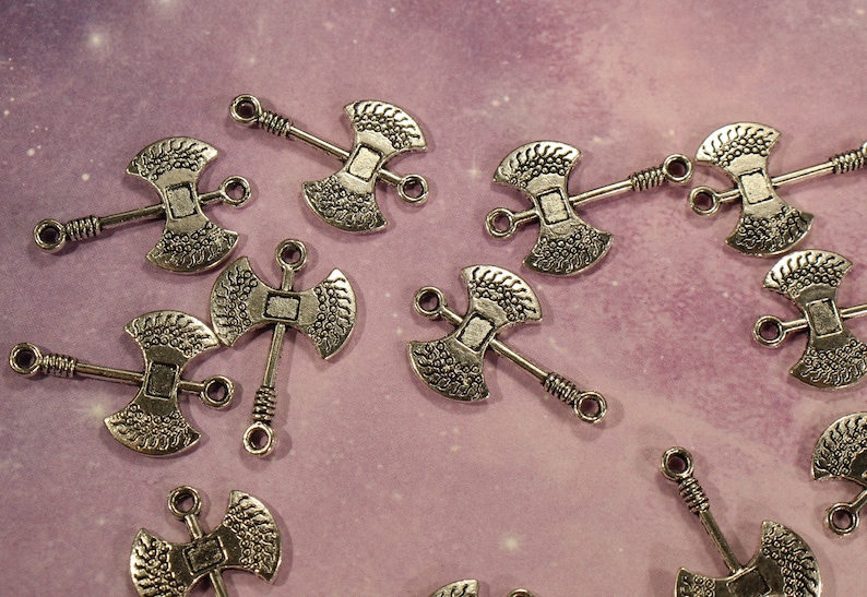 May include: A collection of silver-toned axe charms with intricate details. The charms have a double-sided axe head design with a loop at the top for attaching to jewelry or crafts.
