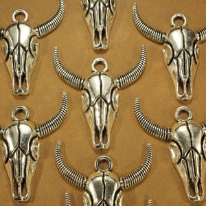 May include: Nine silver-toned bull skull charms with intricate details. Each charm features a detailed skull with horns and a loop for attaching to jewelry or crafts.
