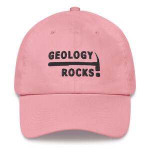 Puede incluir: Gorra de b&eacute;isbol rosa con bordado negro que dice "Geology Rocks!" con un gr&aacute;fico de pico.
