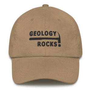 Puede incluir: Una gorra de b&eacute;isbol de color beige con bordado negro que dice "GEOLOGY ROCKS!" con un gr&aacute;fico de un pico.